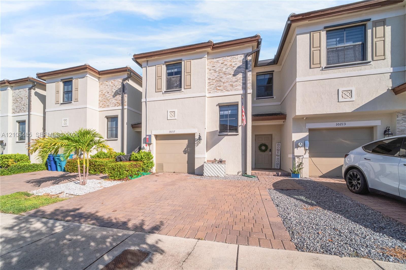Stucco exterior featuring stacked stone accents, paved driveway, attached garage, and decorative exterior shutters