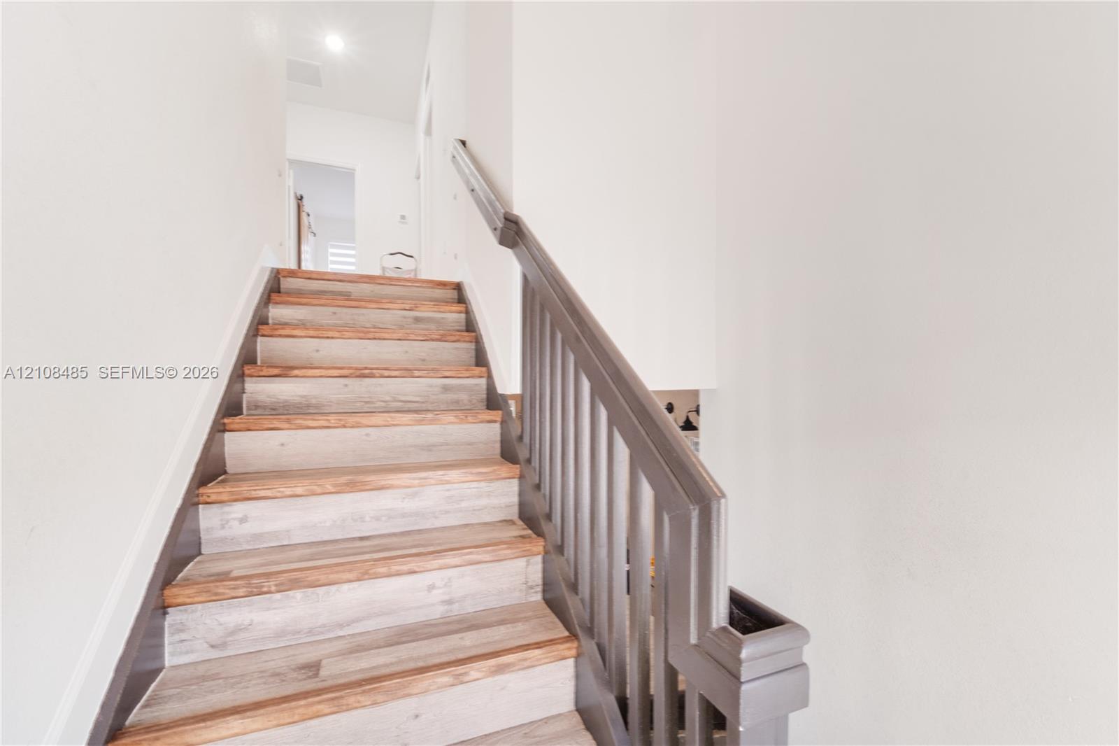 Staircase featuring wood-finish treads and a painted railing with vertical balusters