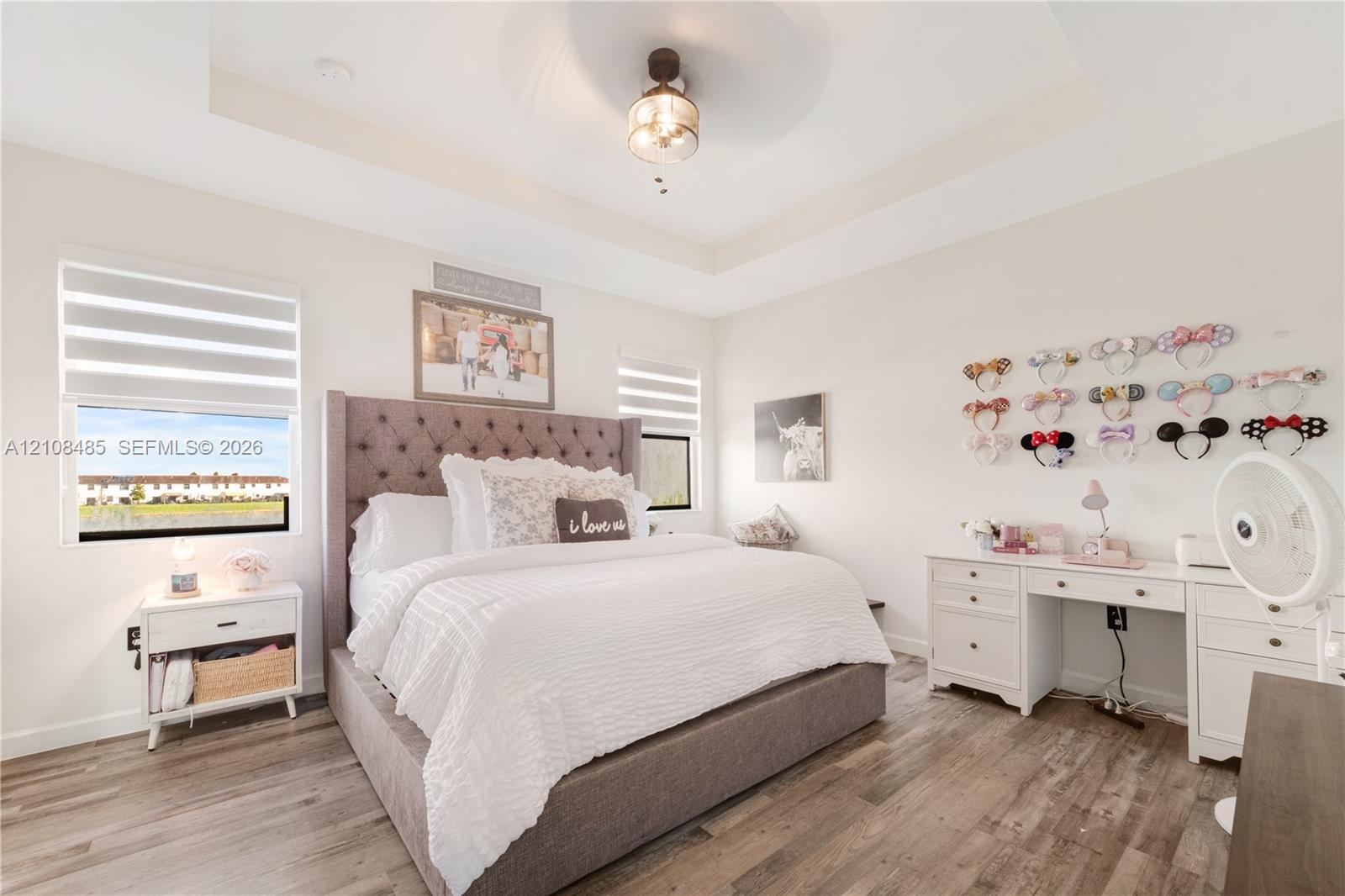 Tray ceiling with center-mounted light fixture, wood-finish flooring, and dual-layered window shades