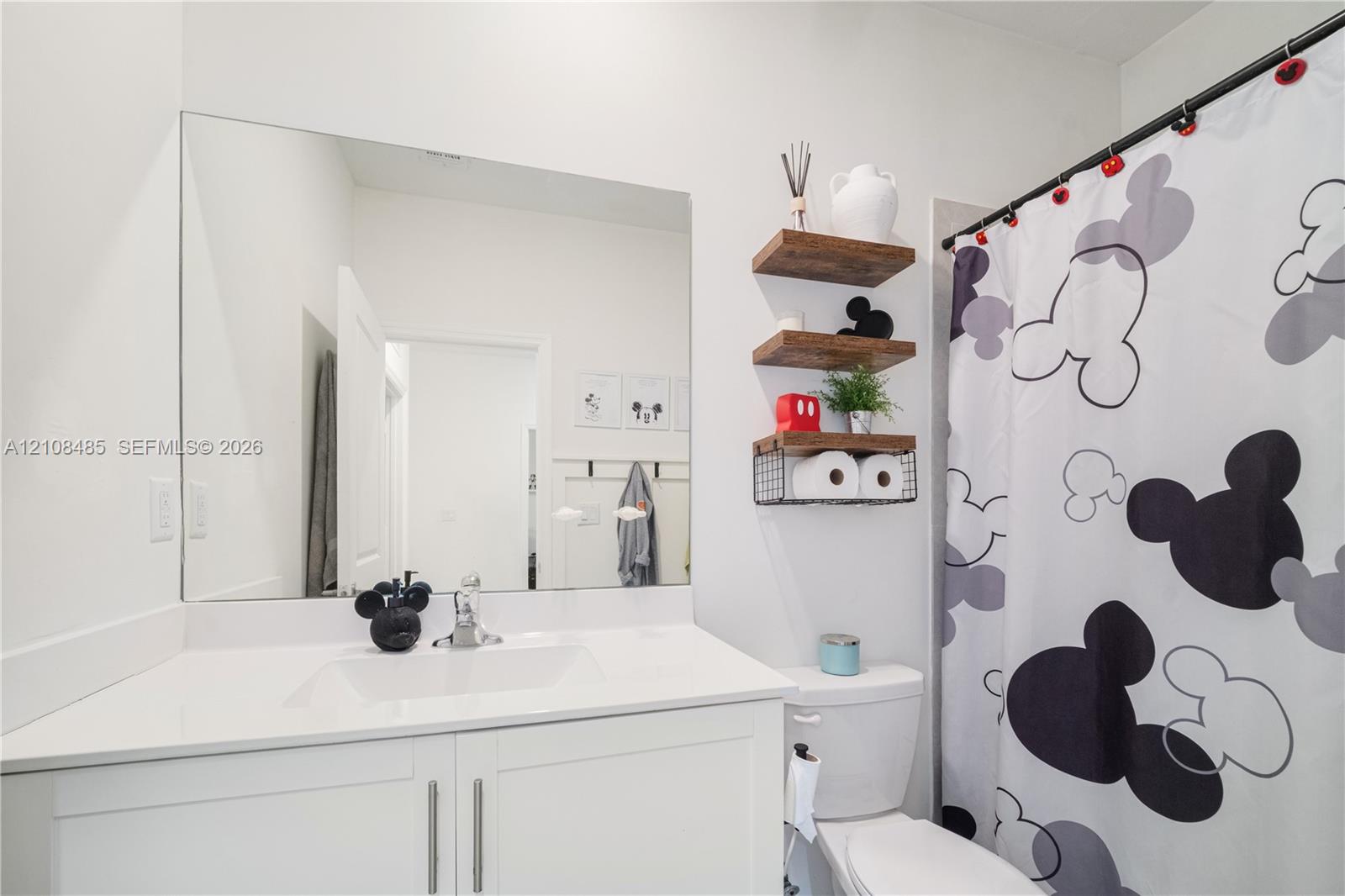 White vanity with a rectangular undermount sink, countertop, and a large frameless wall-mounted mirror