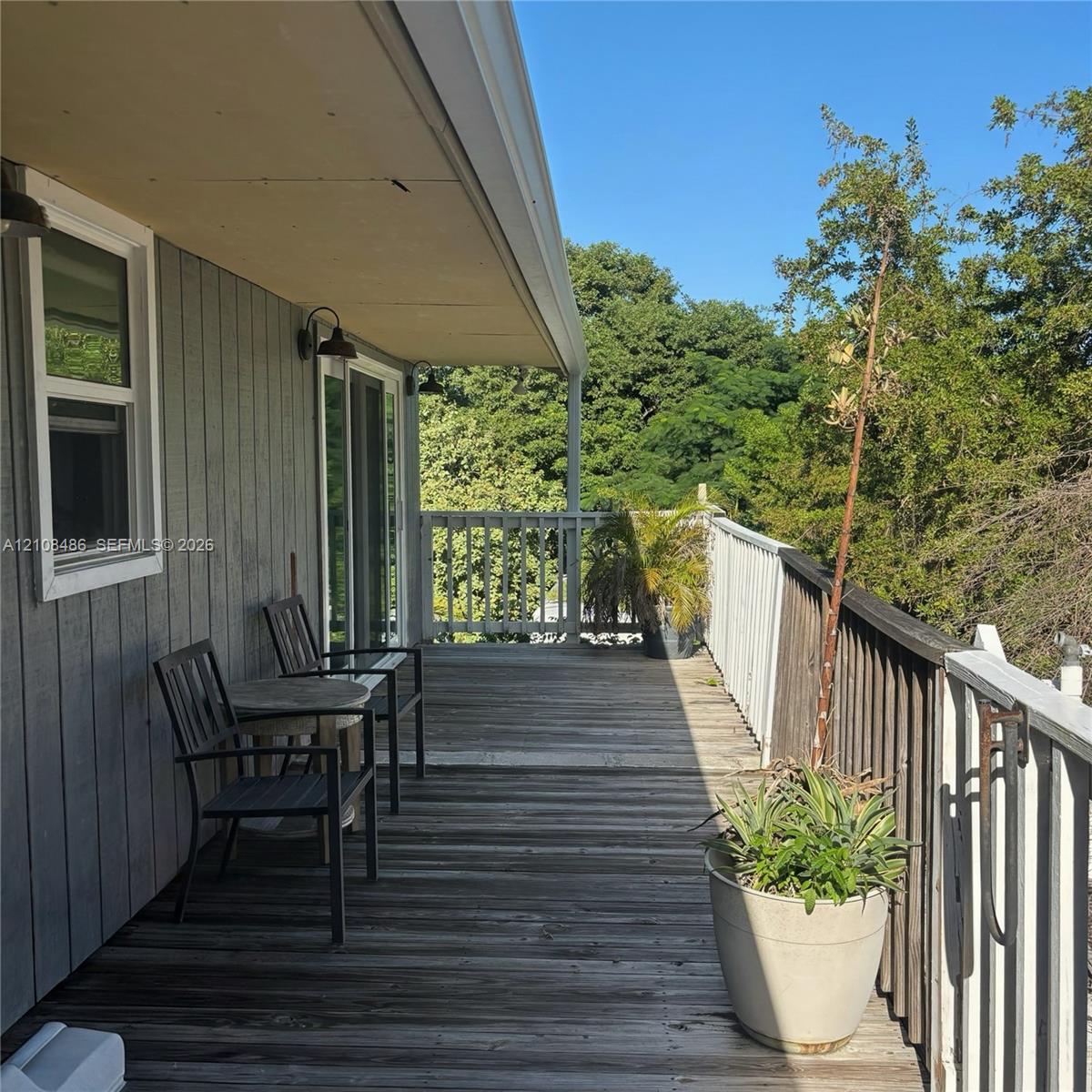 Covered exterior balcony featuring wood-plank decking, vertical wood siding, white railing, and wall-mounted exterior light fixtures