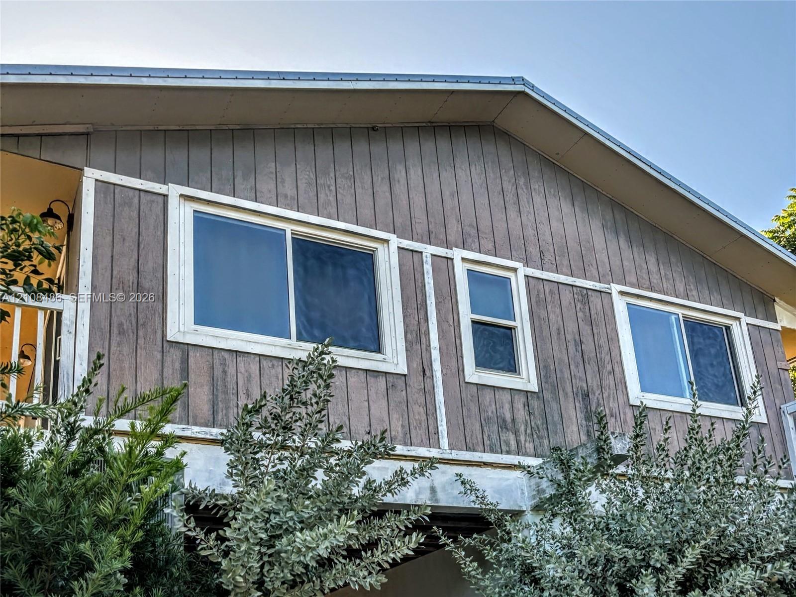 Gabled exterior featuring vertical wood-finish siding, white trim detailing, and multiple sliding windows