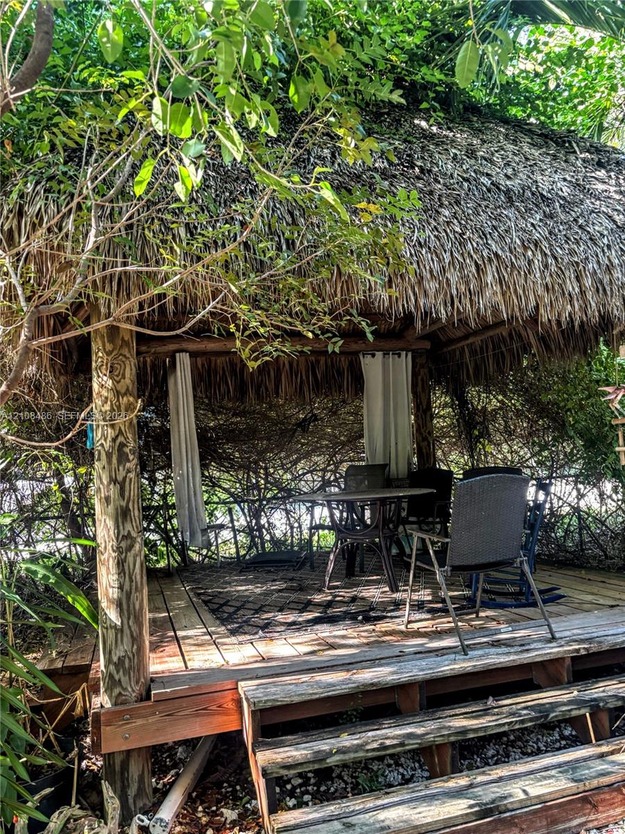 Outdoor structure featuring a thatched roof, wooden post supports, wood-plank decking, and an elevated entrance staircase