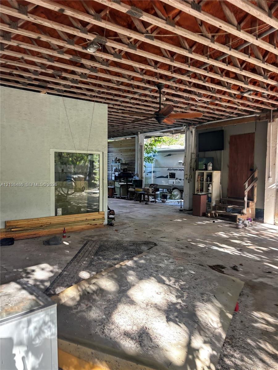 Covered outdoor space featuring an exposed wood truss ceiling, concrete flooring, a ceiling fan, and a wood-frame staircase
