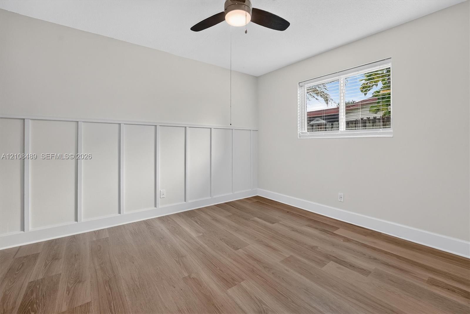 Neutral-toned room featuring wood-finish flooring, white board-and-batten wall detailing, and a central ceiling fan with integrated lighting