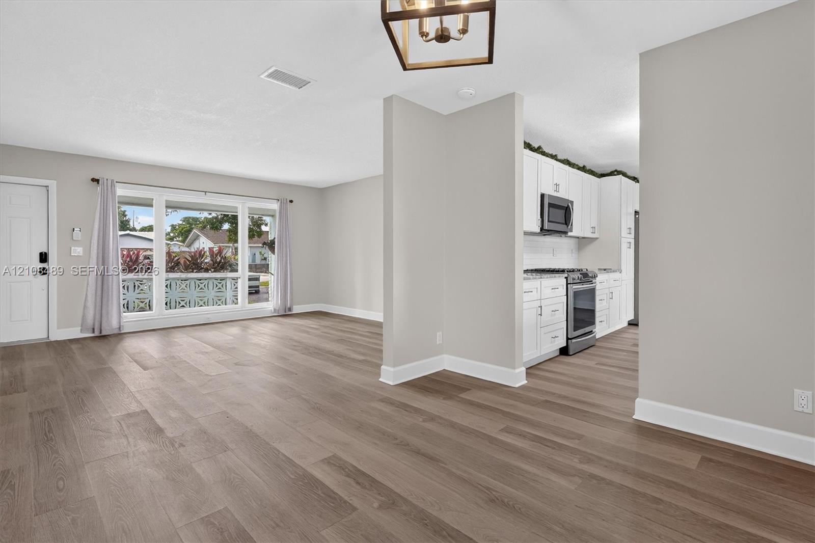Open interior featuring wood-finish flooring, white cabinetry, integrated stainless steel appliances, a picture window, and a geometric pendant light fixture