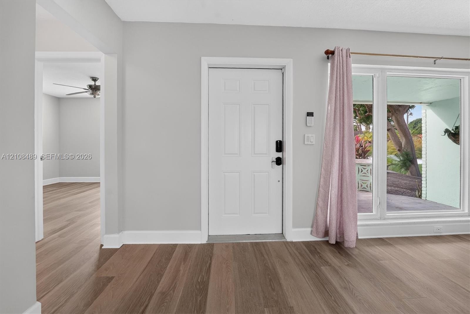 Neutral-toned interior featuring wood-finish flooring, a white six-panel entry door, and expansive glass window panes