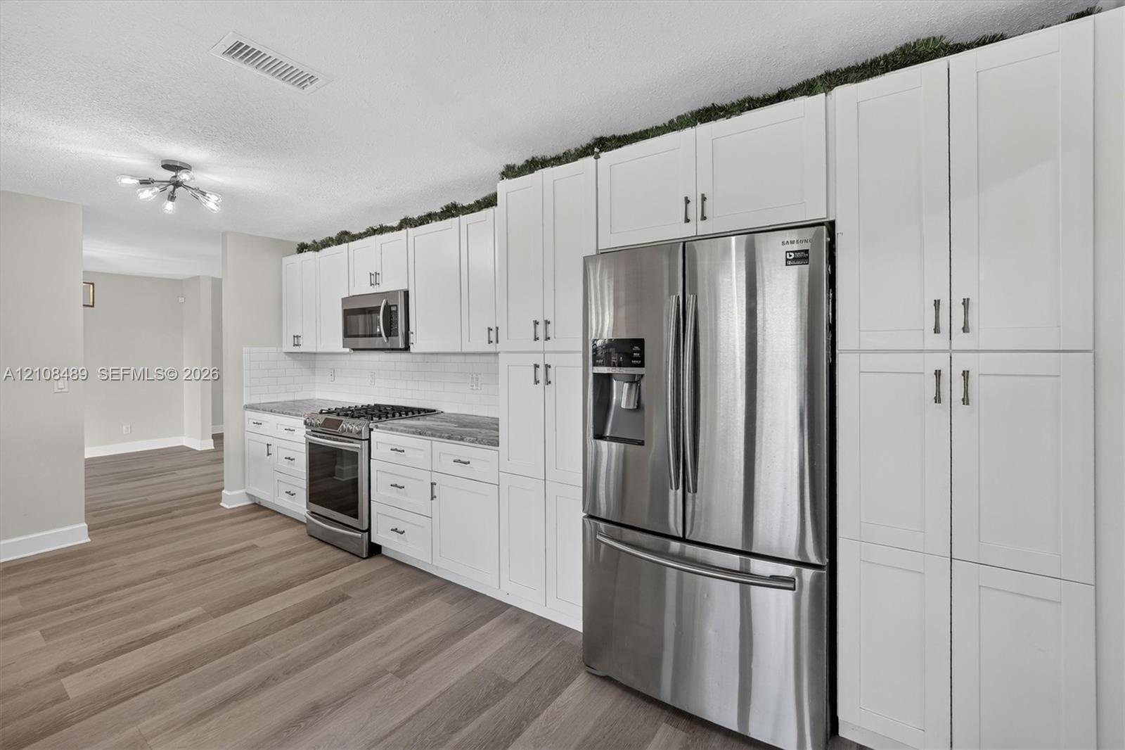 Kitchen featuring white shaker-style cabinetry, stainless steel appliances, stone-finish countertops, subway tile backsplash, and wood-finish flooring