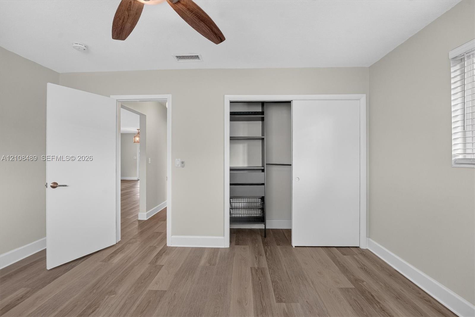 Room featuring wood-finish flooring, a ceiling fan with integrated lighting, and a reach-in closet with built-in shelving