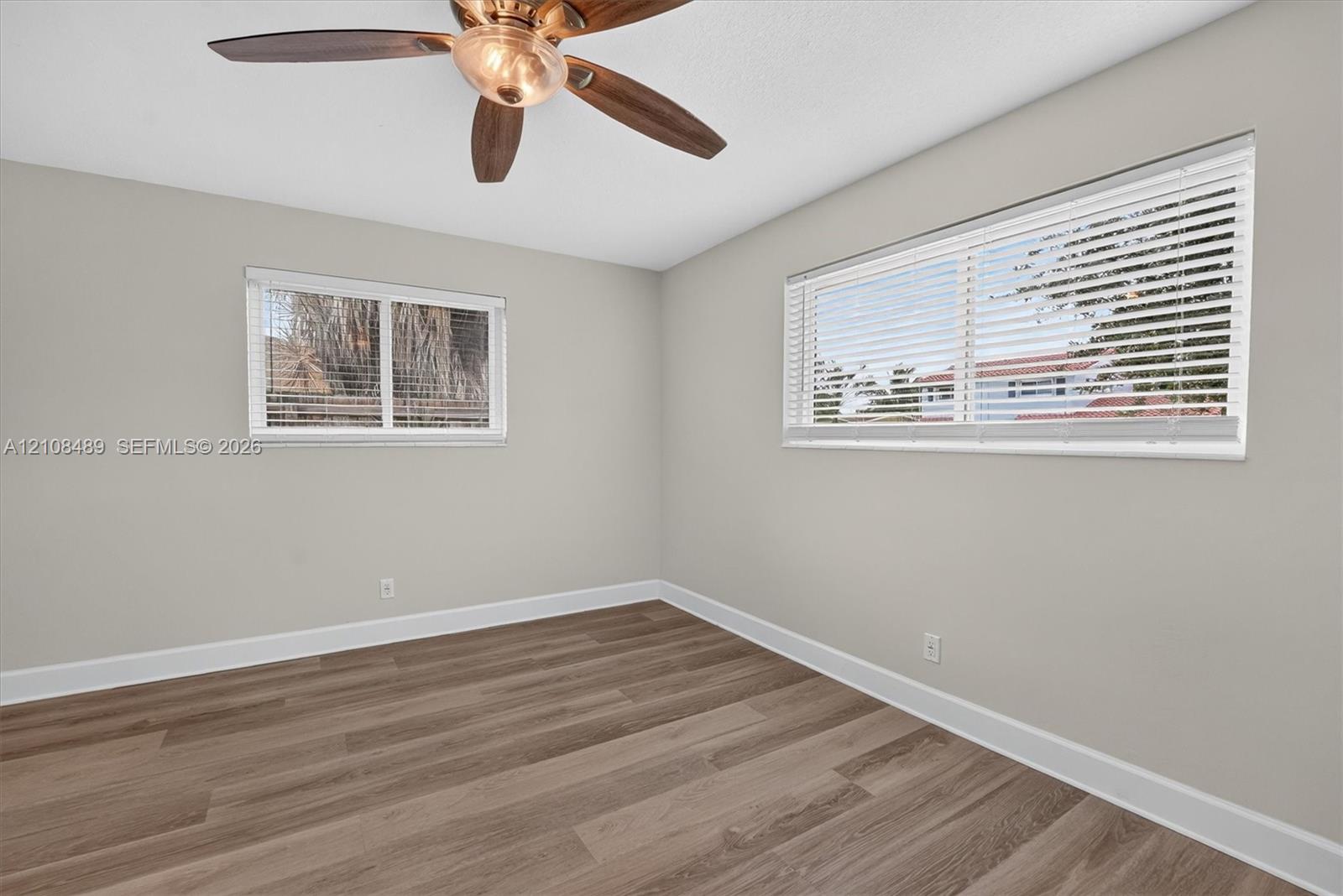 Interior space featuring wood-finish flooring, two dual-pane windows with horizontal blinds, and a multi-blade ceiling fan with integrated light fixture