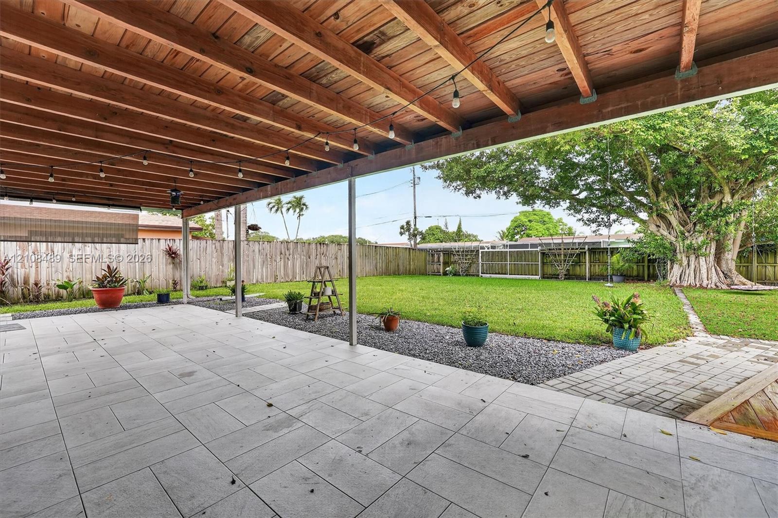 Covered patio featuring a wood-plank ceiling, large-format tile flooring, a fenced backyard, and mature landscaping