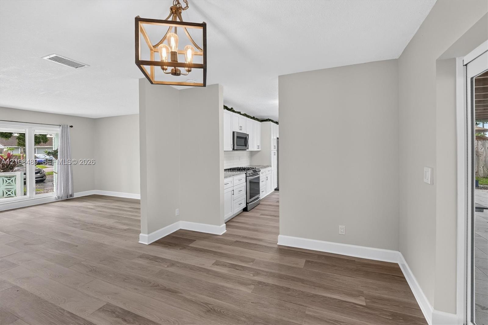 Wood-finish flooring throughout, kitchen featuring white cabinetry and stainless steel appliances, and a geometric metal chandelier