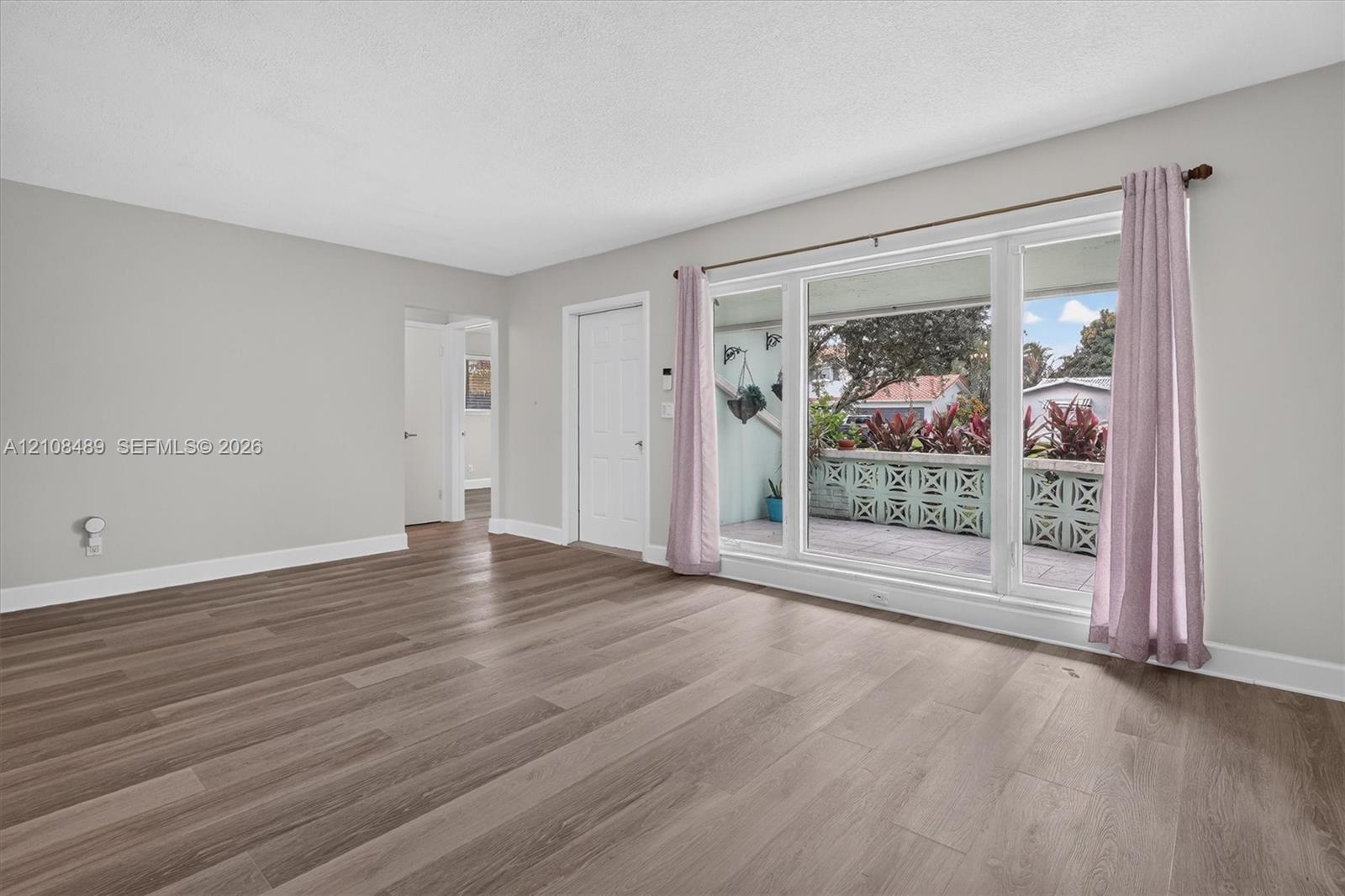 Living area featuring wood-finish flooring, neutral wall paint, and a large multi-pane window with a decorative concrete screen wall exterior