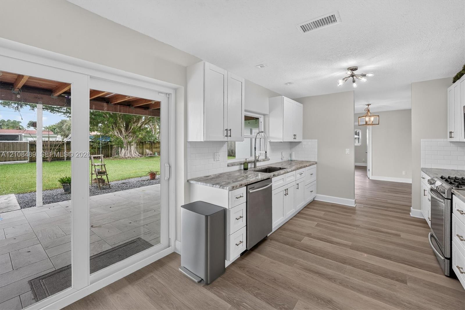 Kitchen featuring white cabinetry, stone-surface countertops, subway tile backsplash, stainless steel appliances, and sliding glass doors to a covered patio
