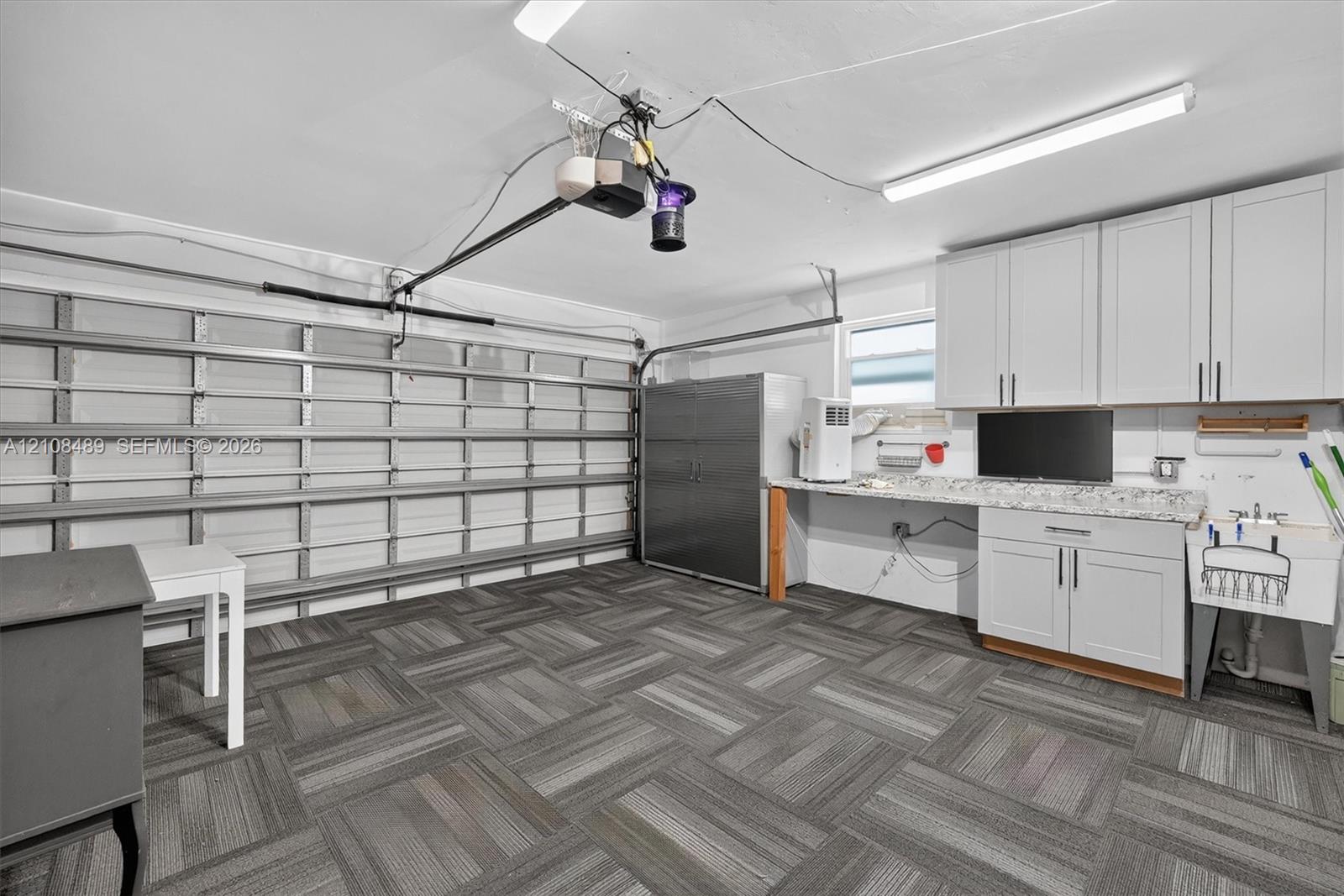 Garage space featuring modular tile flooring, built-in white cabinetry, stone-finish countertops, and a utility sink