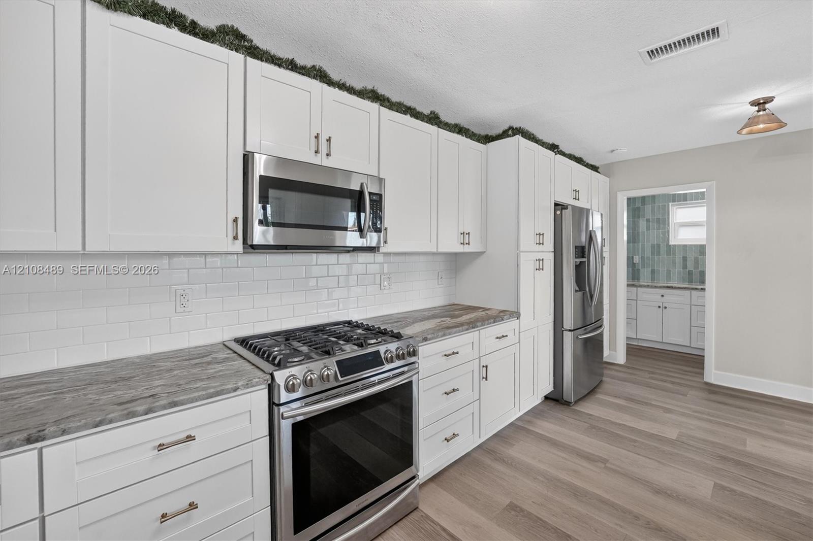 Kitchen featuring white shaker-style cabinetry, stone-patterned countertops, a white subway tile backsplash, stainless steel appliances, and wood-finish flooring