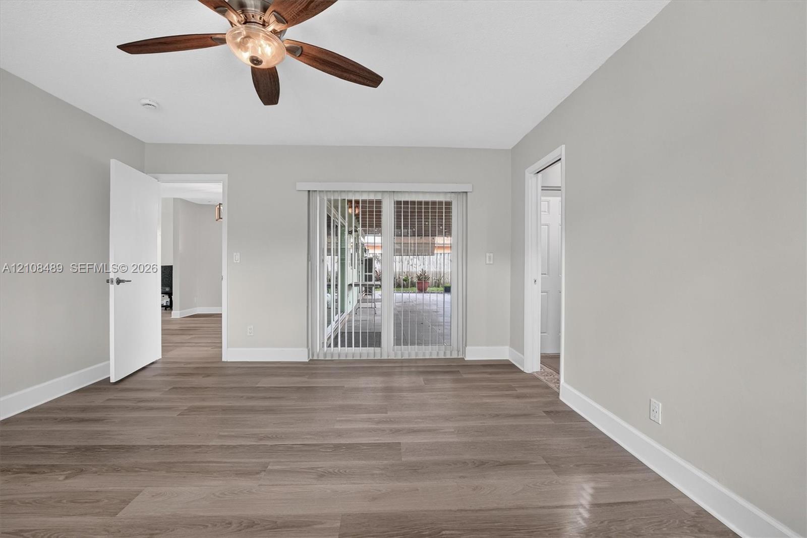 Room featuring wood-finish flooring, ceiling fan with light fixture, and sliding glass doors