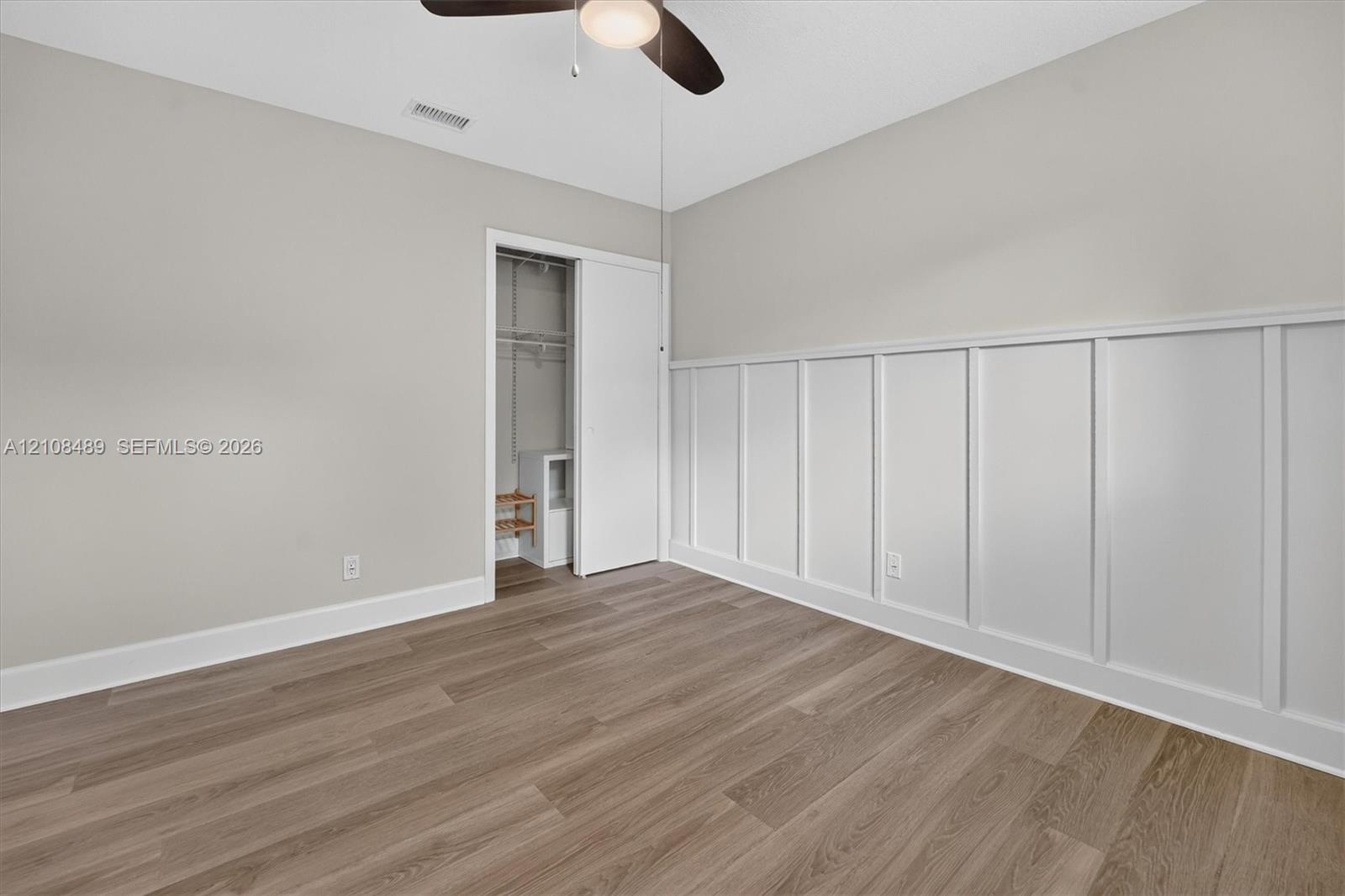 Room featuring wood-finish flooring, white board-and-batten wall detailing, and a ceiling-mounted light fixture with fan