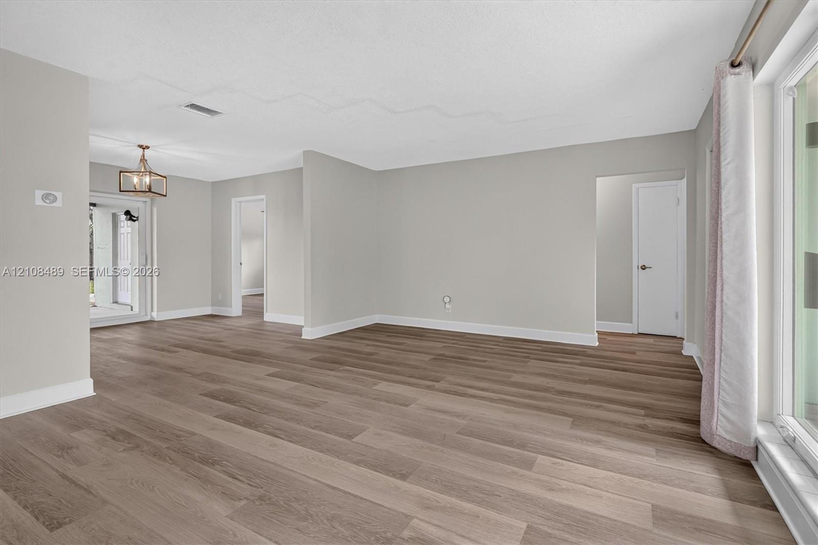 Neutral interior featuring wood-finish flooring, light gray walls, a geometric metal chandelier, and a sliding glass door