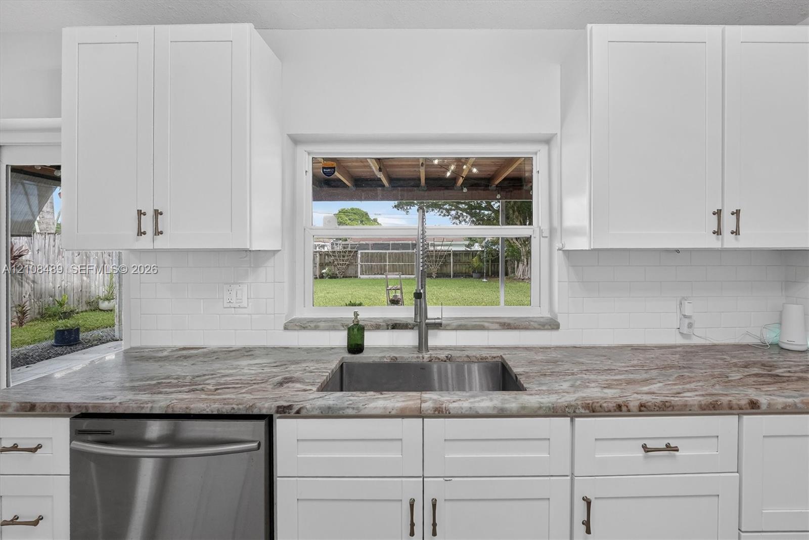 Kitchen featuring white shaker-style cabinetry, stone-patterned countertops, a stainless steel undermount sink with a gooseneck faucet, white subway tile backsplash, and a stainless steel dishwasher