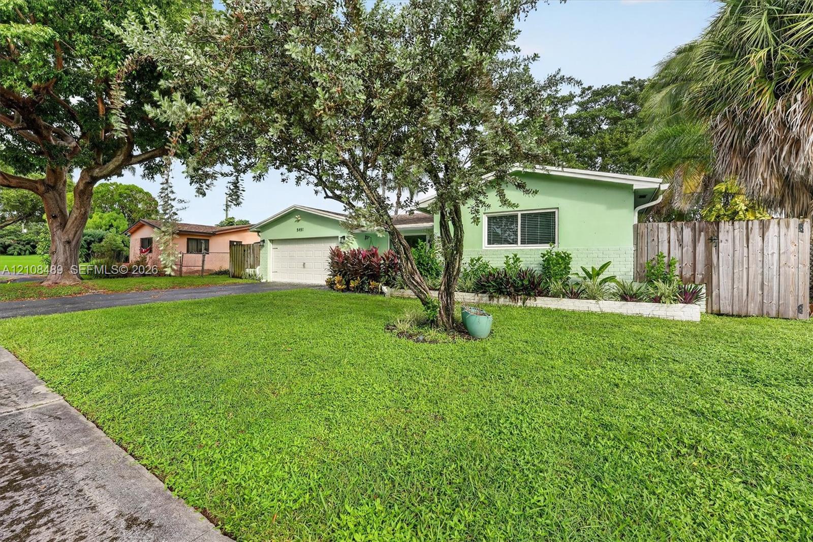 Single-story residence featuring a two-car garage, concrete driveway, front yard landscaping, and vertical wood privacy fencing