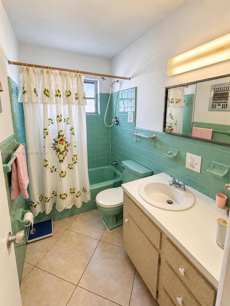 Bathroom featuring ceramic wall tiling, a built-in vanity with a solid-surface countertop and integrated sink, a color-matched bathtub and toilet, and diagonal floor tile
