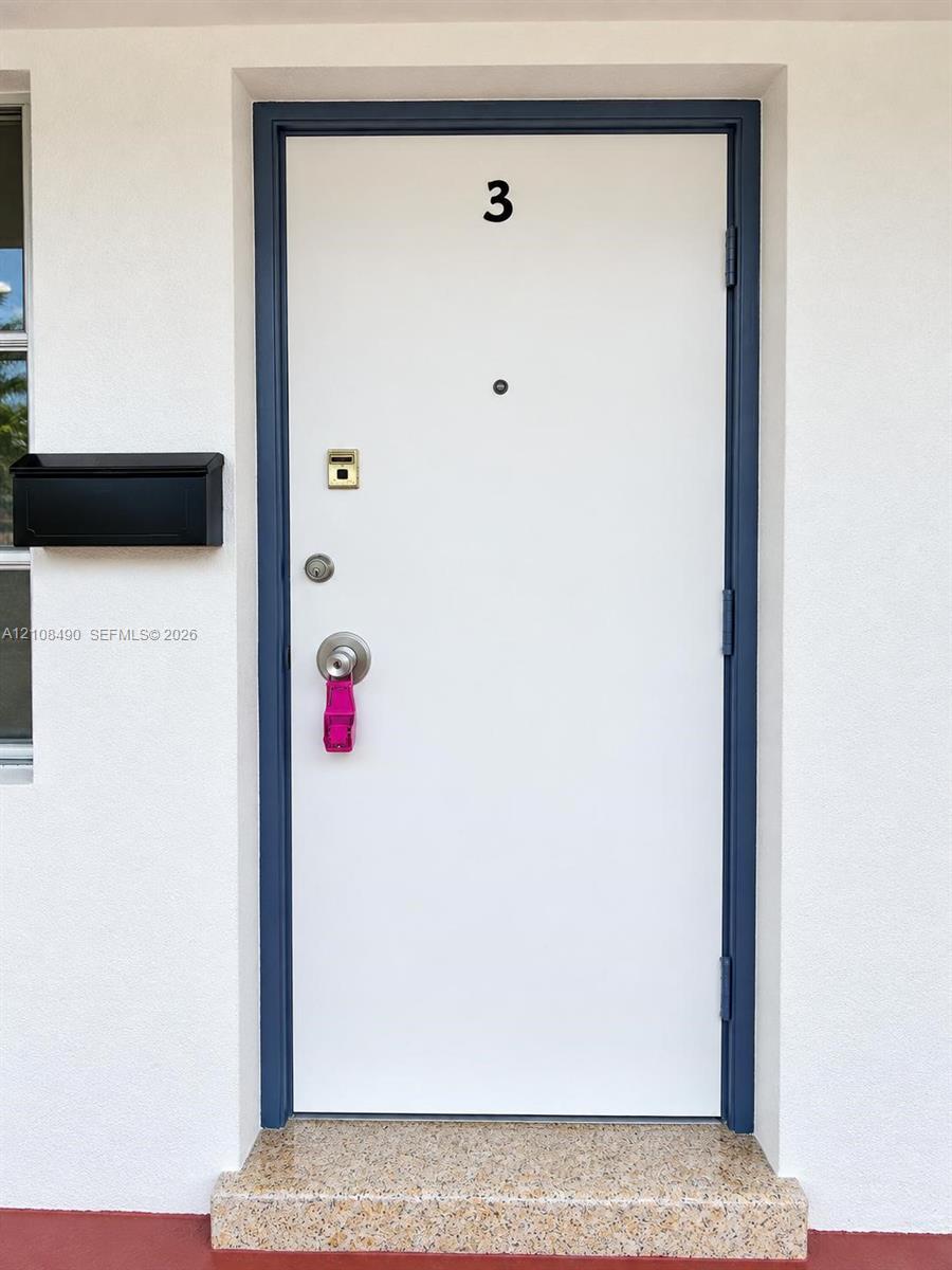 Entry featuring a white door with a dark blue frame, matte black wall-mounted mailbox, and stone-finish threshold