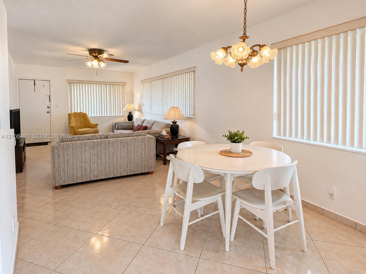 Large-format tile flooring, multi-arm decorative chandelier, ceiling fan with light fixture, and vertical window blinds