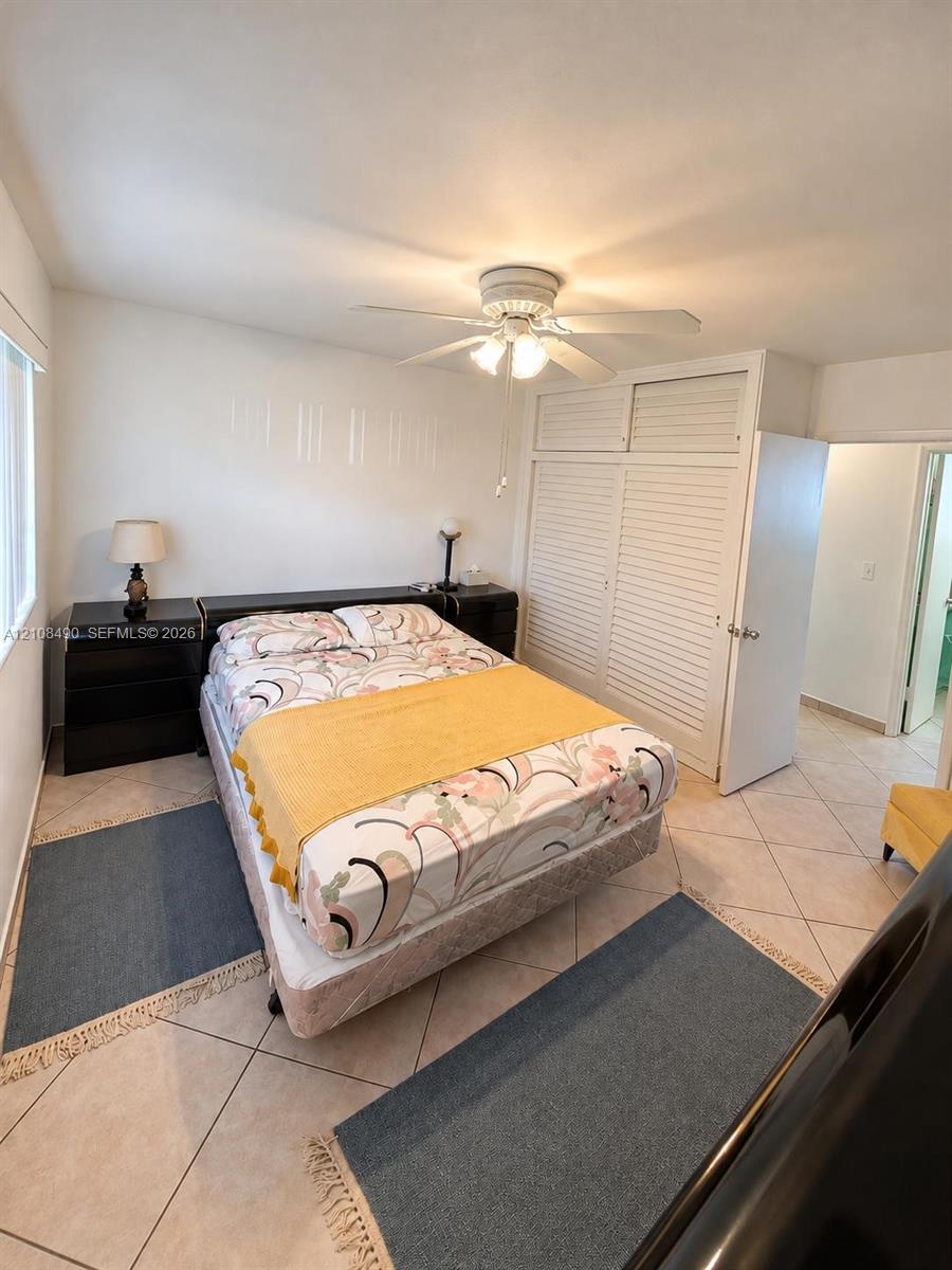 Ceramic tile flooring, built-in floor-to-ceiling closet with louvered doors, and a ceiling fan with integrated light fixture