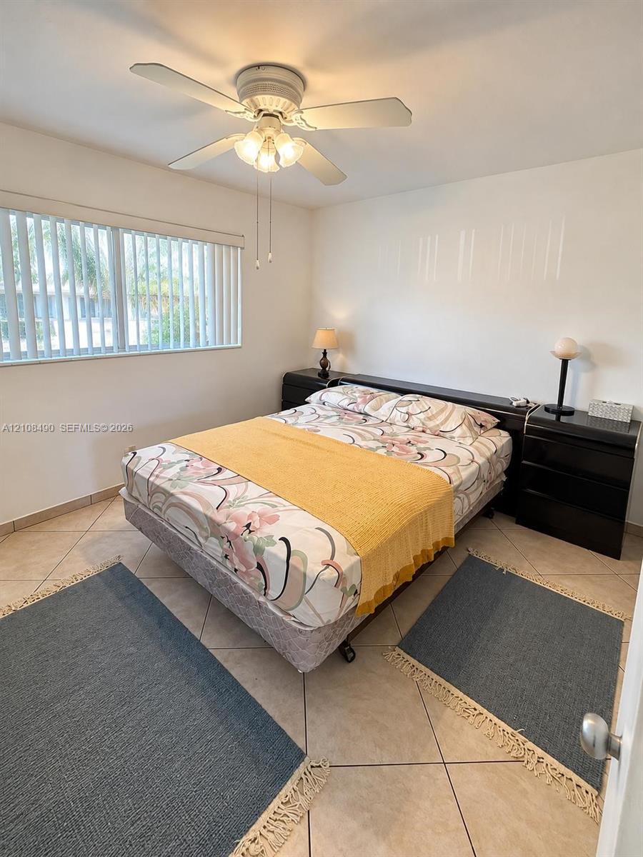 Neutral-toned tile flooring, horizontal blinds, and a white-finish ceiling fan with integrated lighting