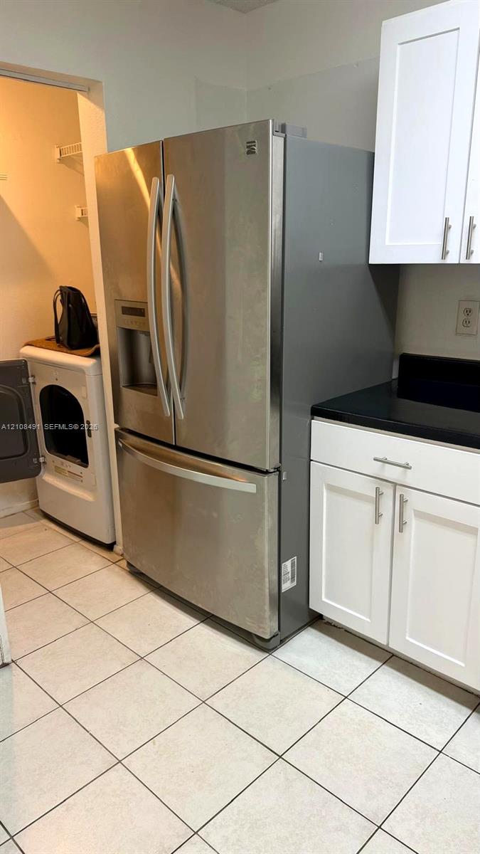 Stainless steel French door refrigerator, white shaker-style cabinetry, dark solid-surface countertops, and ceramic tile flooring Stainless steel French door refrigerator, white shaker-style cabinetry, dark solid-surface countertops, and ceramic tile flooring