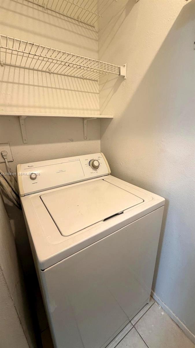 Dedicated laundry area featuring a top-load washer, installed wire shelving, and tiled flooring