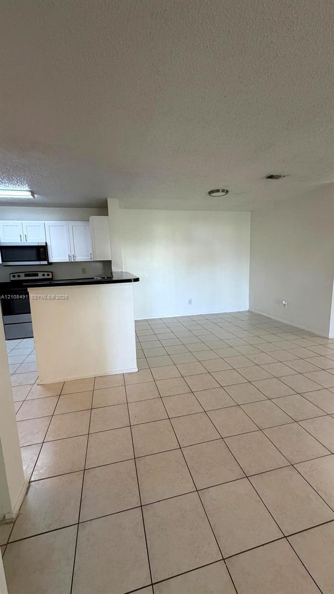 Open-concept interior featuring light-toned tile flooring, recessed ceiling lighting, and a kitchen peninsula with a dark countertop Open-concept interior featuring light-toned tile flooring, recessed ceiling lighting, and a kitchen peninsula with a dark countertop