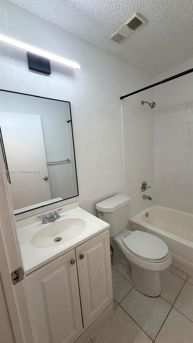 Bathroom featuring a vanity with a white integrated countertop, wall-mounted light fixture, rectangular mirror with a black frame, tile flooring, and a tub-shower combination with tile surround