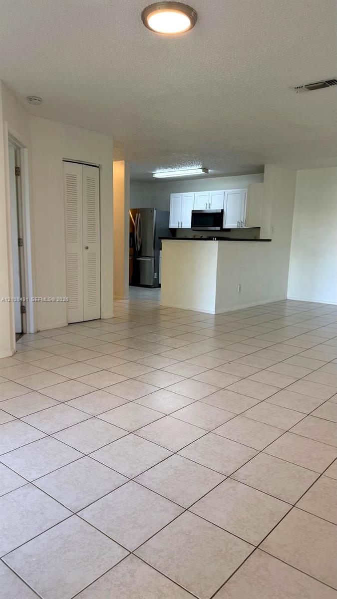 Open-concept interior featuring neutral tile flooring, white cabinetry, integrated stainless steel appliances, and a breakfast bar Open-concept interior featuring neutral tile flooring, white cabinetry, integrated stainless steel appliances, and a breakfast bar