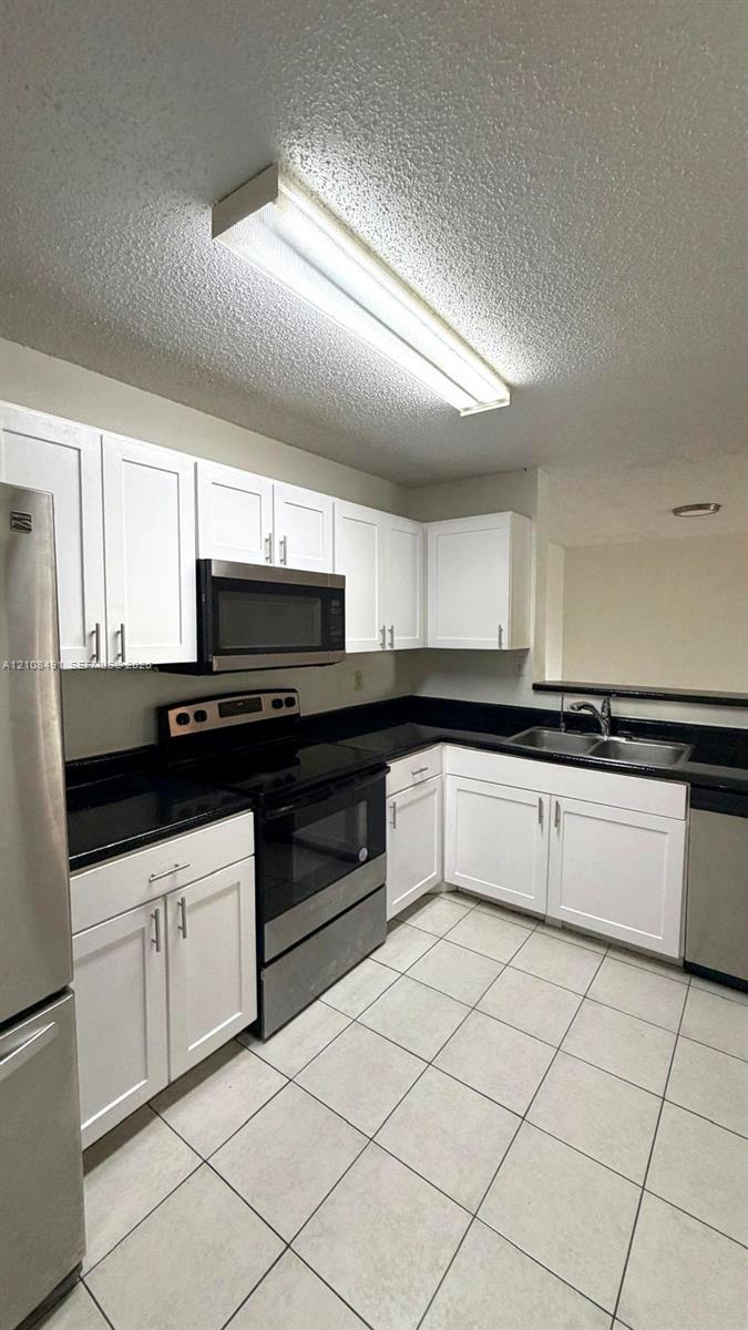 White shaker-style cabinetry, dark solid-surface countertops, stainless steel appliances, dual-basin stainless steel sink, and ceramic tile flooring White shaker-style cabinetry, dark solid-surface countertops, stainless steel appliances, dual-basin stainless steel sink, and ceramic tile flooring