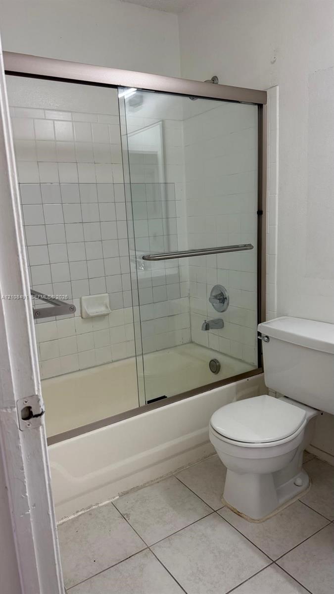 Bathtub with sliding glass enclosure, white tile surround, integrated soap dish, and porcelain toilet