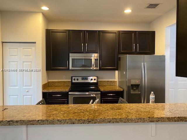 Kitchen featuring dark wood cabinetry, stone countertops, stainless steel appliances, and recessed ceiling lighting