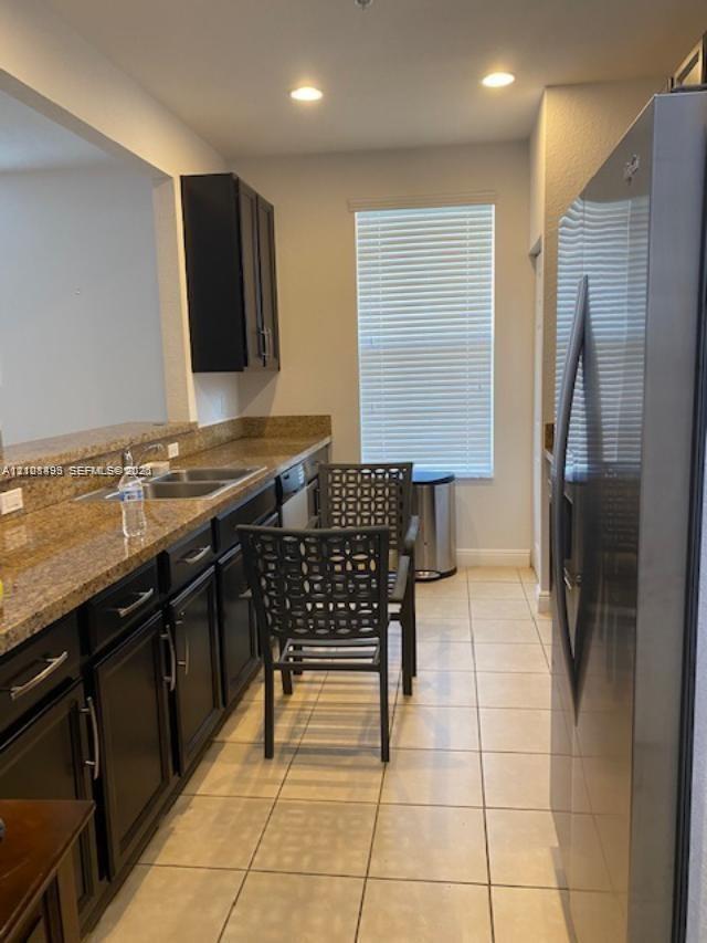 Kitchen featuring dark-finish cabinetry, stone countertops, double-basin stainless steel sink, recessed lighting, and tile flooring