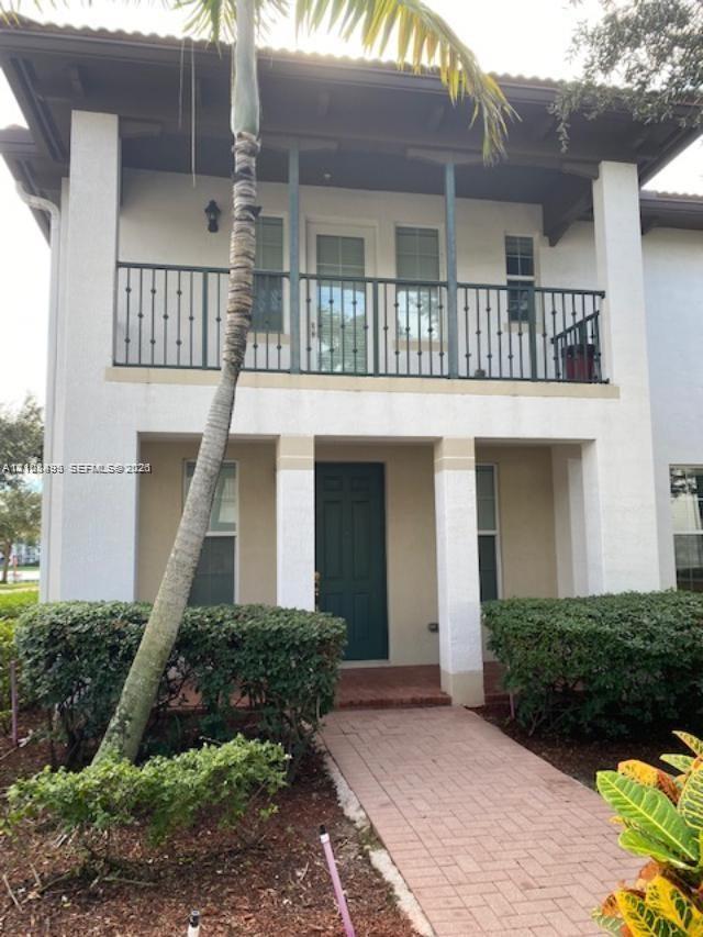 Two-story exterior featuring a second-level balcony with metal railing, a covered entryway, a brick-paver walkway, and structural support columns