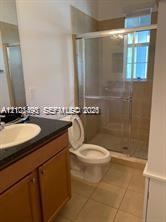 Bathroom featuring wood-finish cabinetry, dark countertop, drop-in sink, and a glass-enclosed shower with tile surround