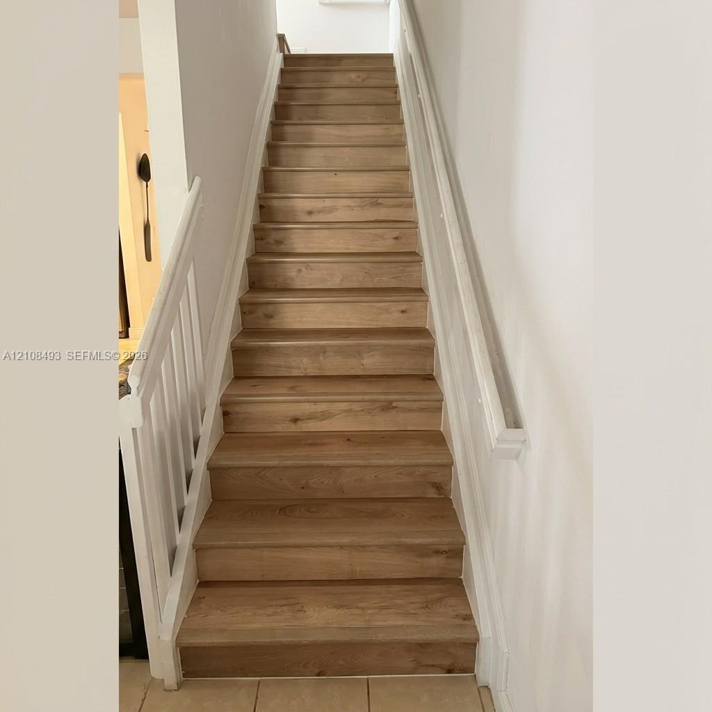 Staircase featuring wood-finish treads, white vertical balusters, and a wall-mounted handrail