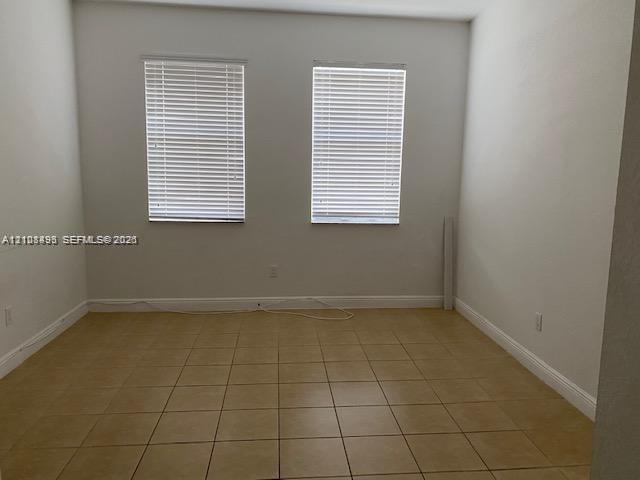 Interior space featuring ceramic tile flooring, neutral wall tones, and two windows equipped with horizontal blinds