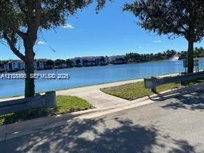 Waterfront property featuring a paved walking path, mature trees, and grass landscaping