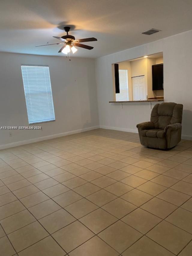Neutral tile flooring, ceiling fan with light fixture, window with horizontal blinds, and a built-in pass-through window with counter ledge