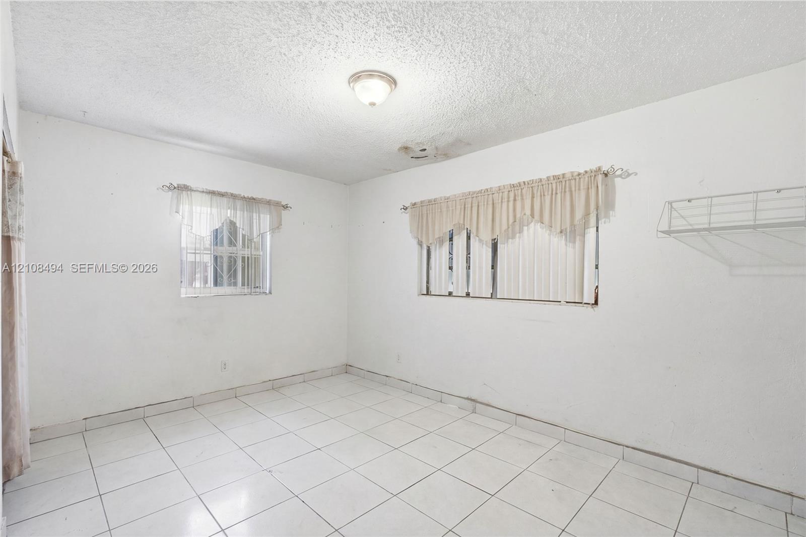 Interior space featuring white floor tiles, a dual-window configuration, a flush-mount ceiling light fixture, and a built-in wire wall shelf