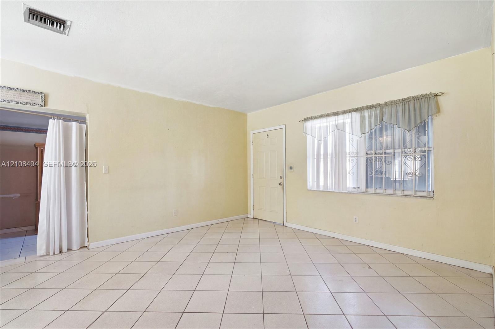 Interior space featuring diagonal-patterned ceramic tile flooring, neutral wall paint, and a window equipped with metal security bars Interior space featuring diagonal-patterned ceramic tile flooring, neutral wall paint, and a window equipped with metal security bars