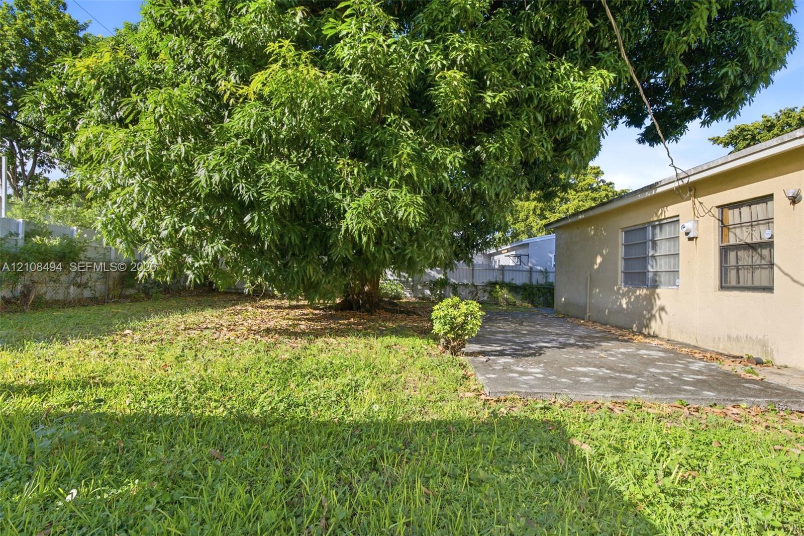 Backyard featuring a mature tree, concrete patio, grass lawn, and perimeter fencing