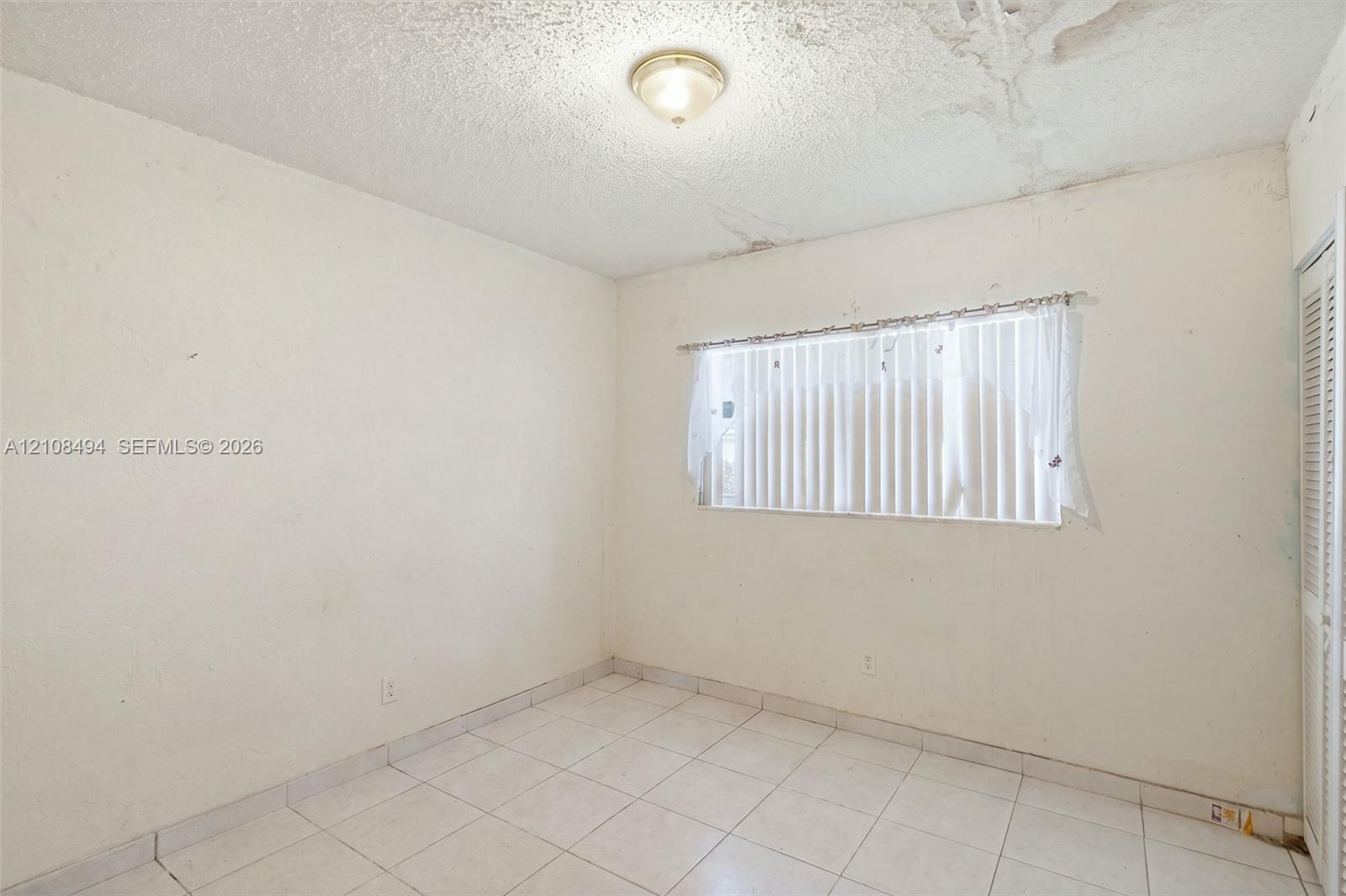 Room featuring white tile flooring, ceiling-mounted flush lighting, and a louvered bi-fold closet door