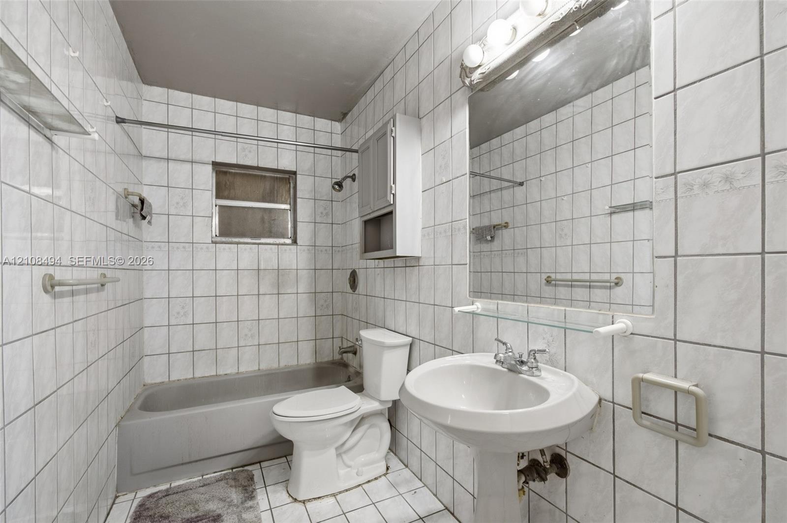 Full-height tile wall surround, white pedestal sink, integrated wall-mounted medicine cabinet, wall-to-wall mirror with glass shelving, and porcelain tub with shower head fixture